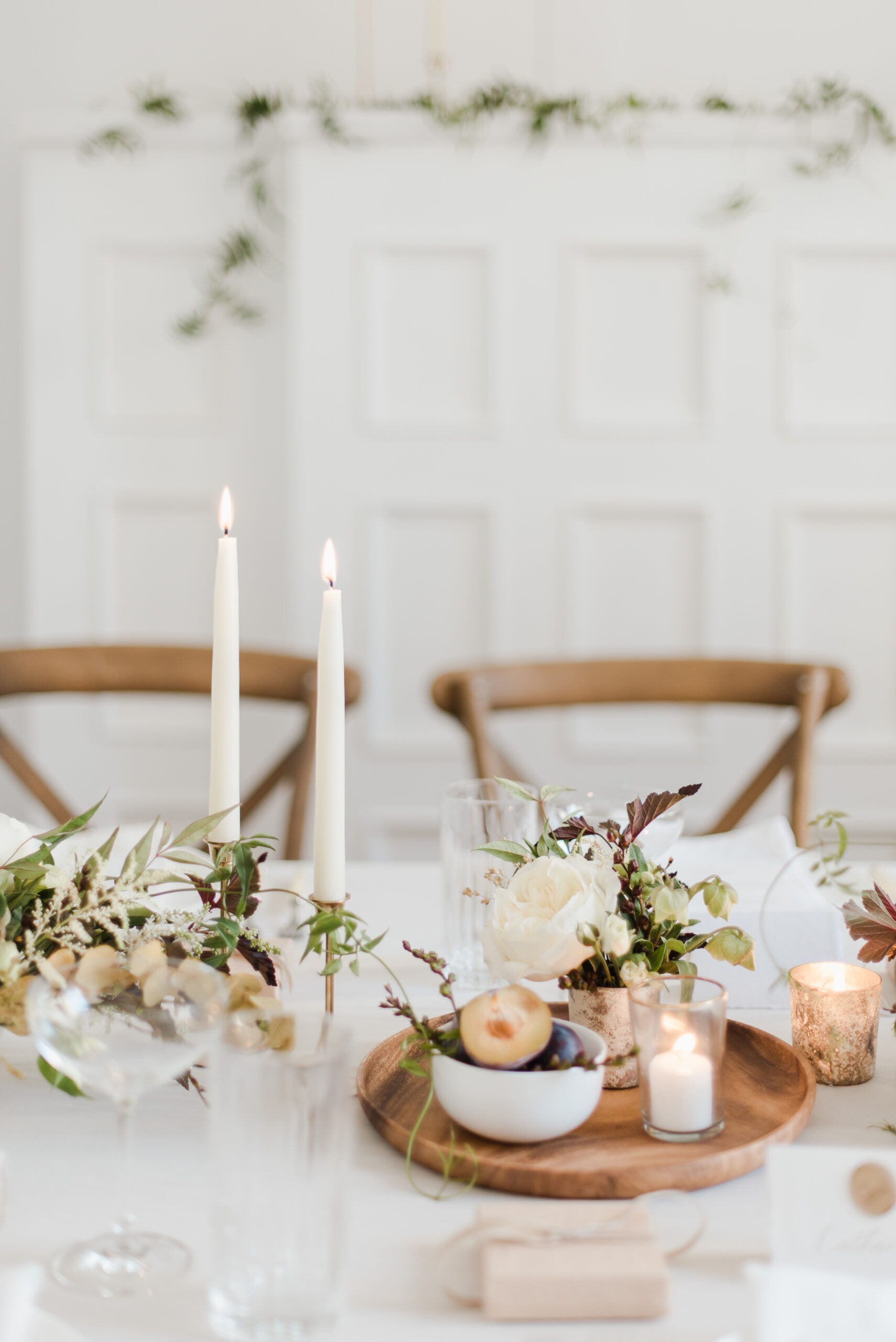 Elegant dining table styled with white flowers, taper candles, glassware, and natural greenery for a refined celebration.